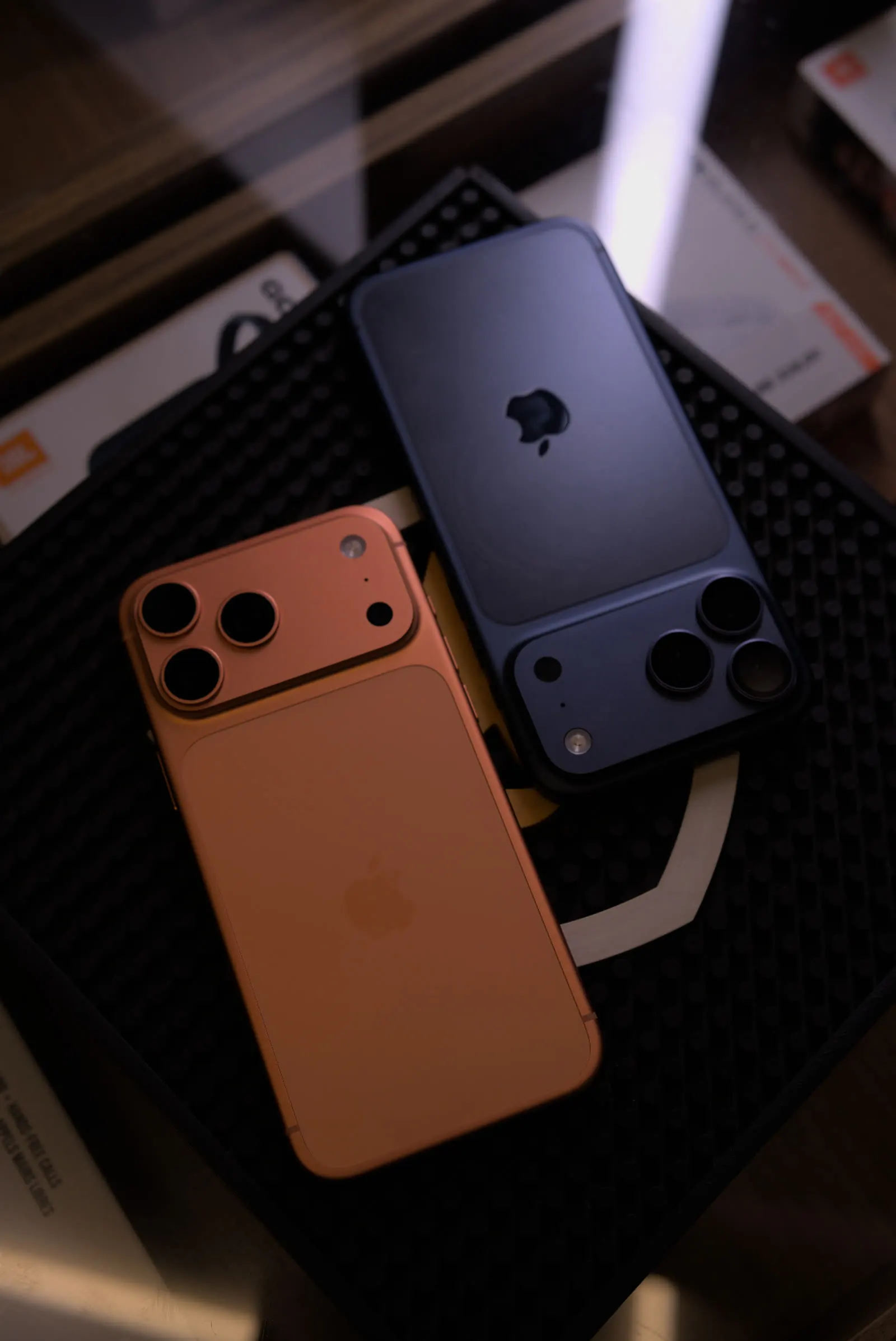 iPhones Pro em laranja e azul sobre superfície escura.